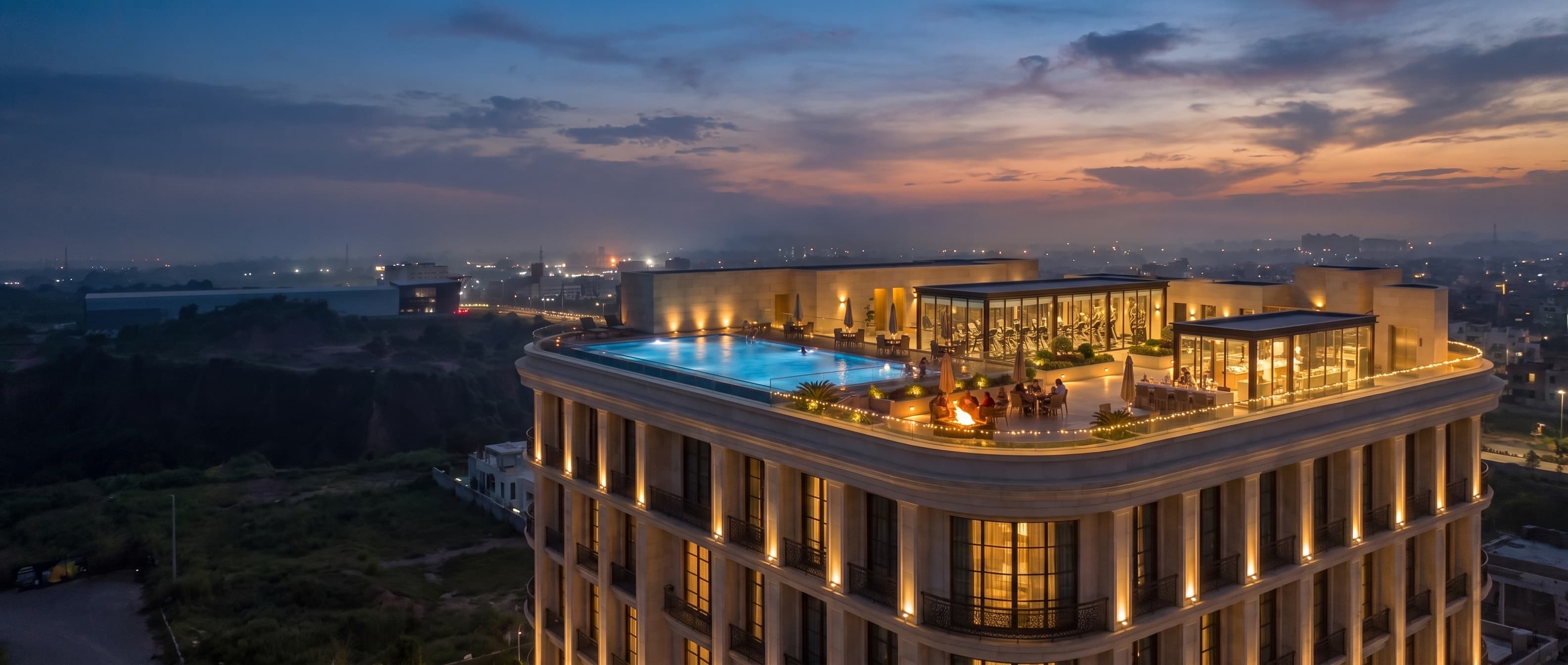 The Afsons One at dusk from the air, the lit rooftop deck with its pool, gym pavilion and fire pit crowning the building