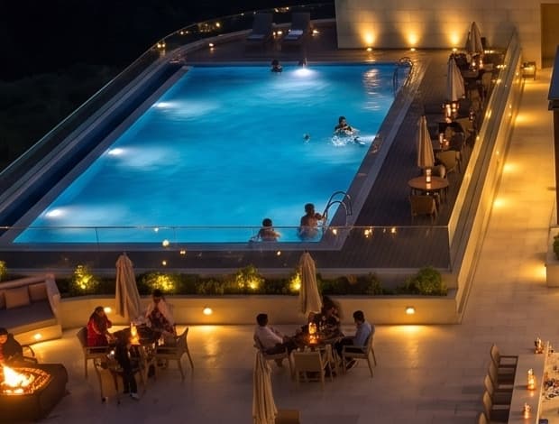 The rooftop pool lit at night, with poolside seating along its edge