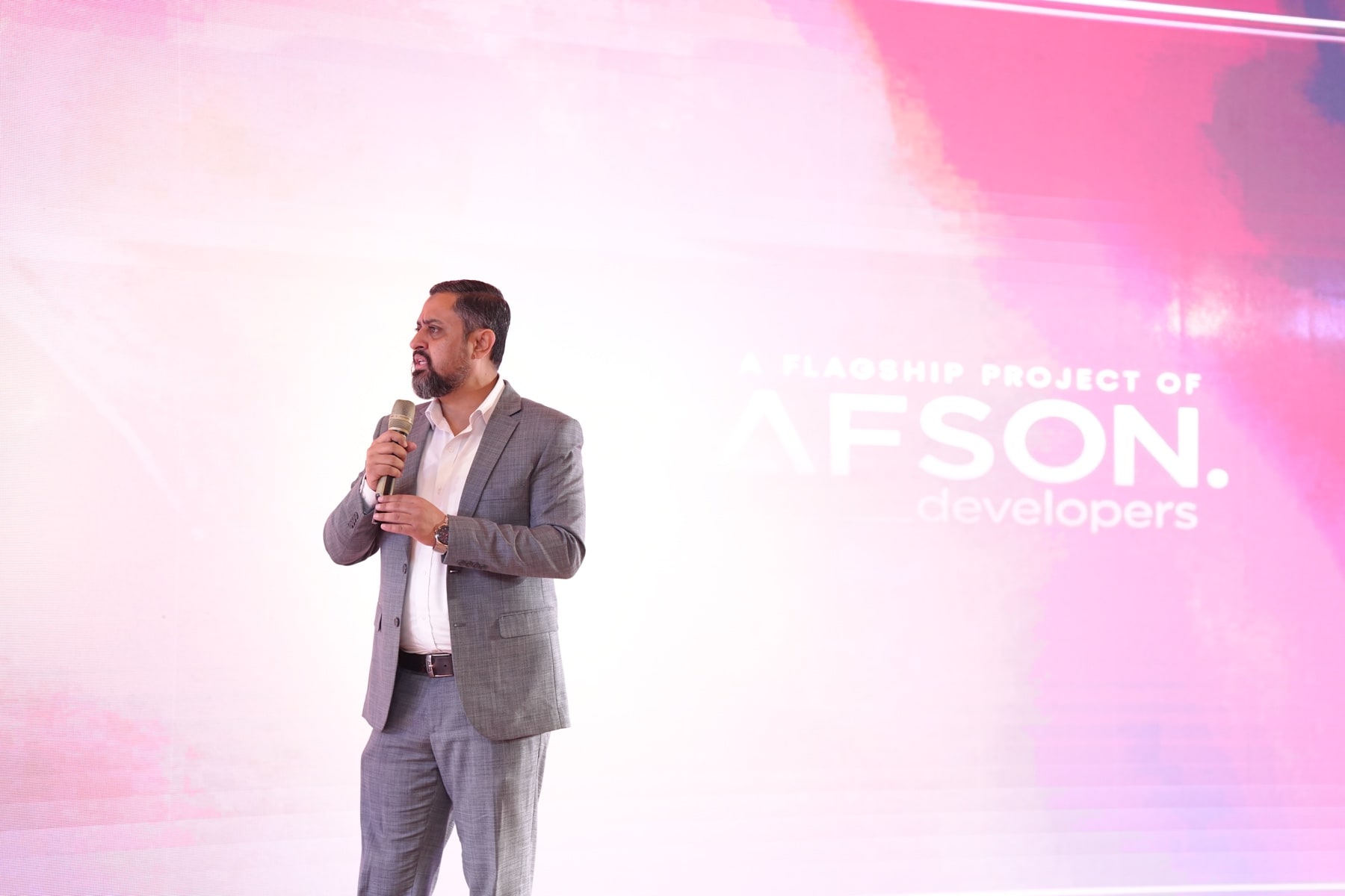 A speaker presenting on stage in front of the screen reading a flagship project of Afson Developers