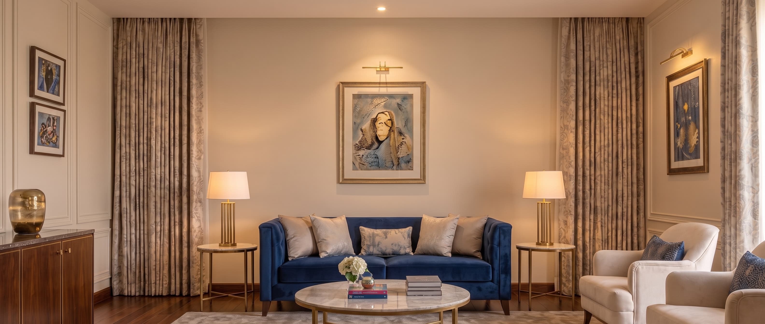 An apartment living room: blue velvet sofa between brass lamps, framed art above, curtains to the floor